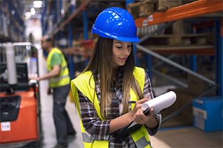 Female engineer in safety equipment doing inventory in a warehouse.