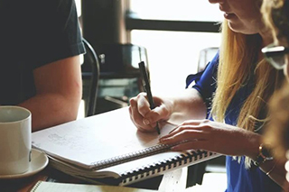 Business woman taking notes on a marketing team brainstorming meeting in a coffee shop.