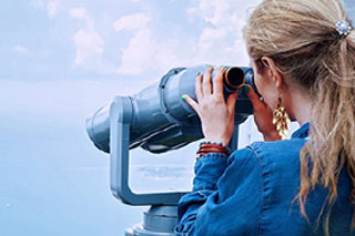 Girl at an overlook looking through binoculars at water on a low visibility day.